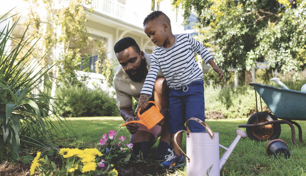 A father and son watering flowers together in a garden